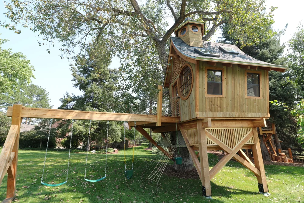 Wooden backyard treehouse with a roof, swing beam and safety railings